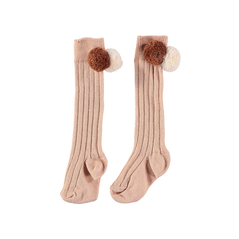 Dust rose knee length rib socks with two pom poms in beige and brown. Brand: Búho Details: Ribbed, Two pom-poms on each side Composition: 79% Cotton, 18% Polyamide, 3% Lycra Made in: France